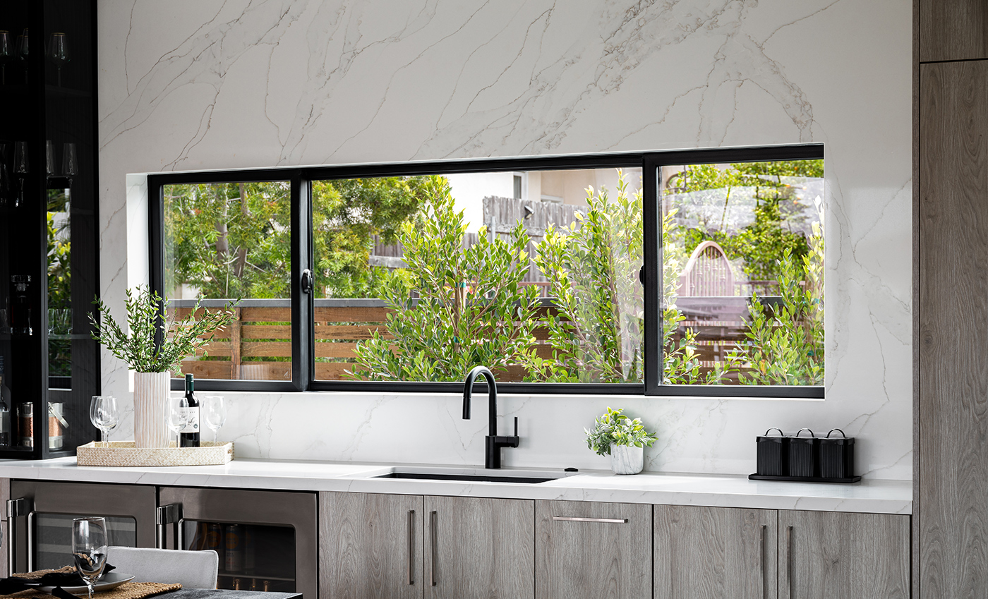 A kitchen with an extra-wide Andersen® 100 Series Gliding Window installed into a marble backsplash above the sink.