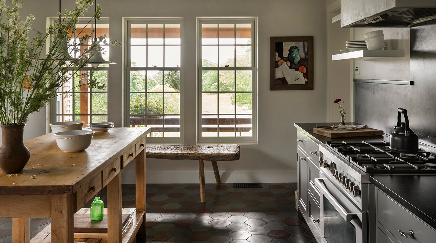 A charming country kitchen with a wood work table, stone floors, slate countertops and Andersen® A-Series Double-Hung Windows. 