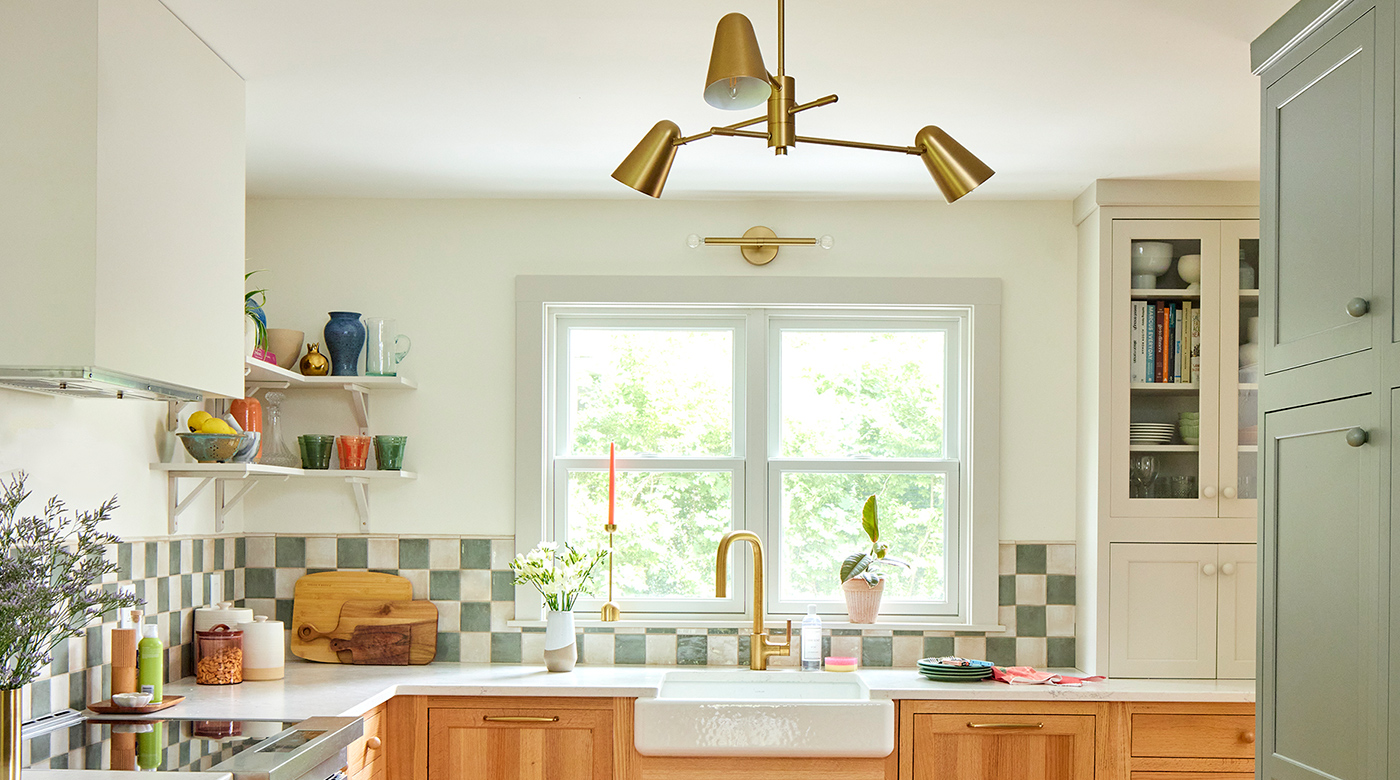 A kitchen with checkerboard backsplash, warm wood cabinetry and floors, and Andersen® 200 Series Double-Hung Windows above the kitchen sink.