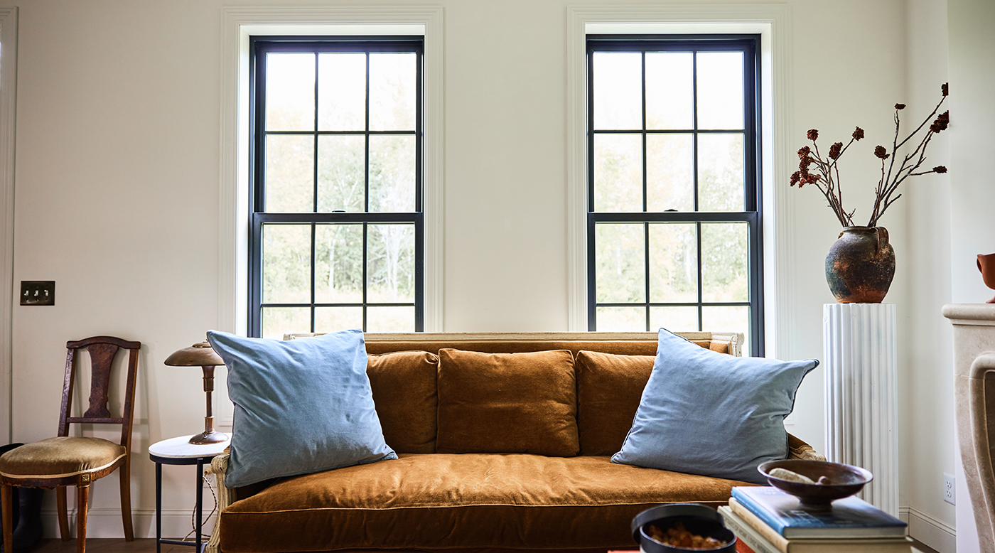 A bright and airy living room with black Andersen® 100 Series Double-Hung Windows featuring a colonial grille pattern.