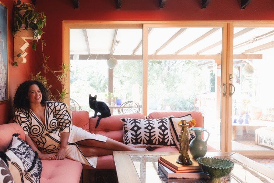 Justina Blakeney and her cat lounge on a rose-colored couch on her lanai which connects to the courtyard outside via an E-Series Gliding Patio Door.