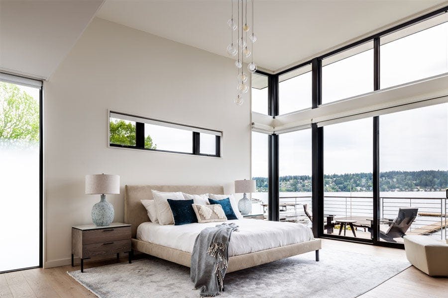 A bedroom with a full wall of glass that wraps around the corner and showcases a lake view.
